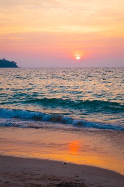 denizde gün batımı. kumlu plaj, berrak su, dalgalar. batan güneşin sıcak renklerde sörf hattı.