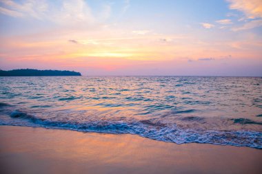 denizde gün batımı. kumlu plaj, berrak su, dalgalar. batan güneşin sıcak renklerde sörf hattı.