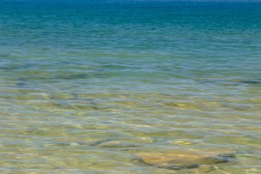 Mavi ve turuncu berrak su dokusu. Okyanusun arka planı ve güneş tarafından aydınlatılan deniz. Yumuşak dalgalar. Doğal su.