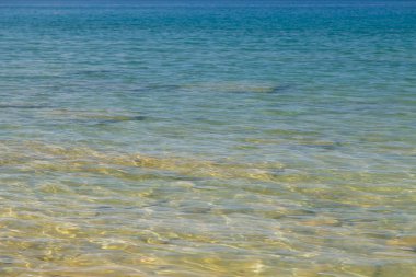 Mavi ve turuncu berrak su dokusu. Okyanusun arka planı ve güneş tarafından aydınlatılan deniz. Yumuşak dalgalar. Doğal su.