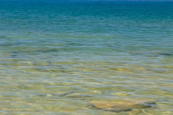 Mavi ve turuncu berrak su dokusu. Okyanusun arka planı ve güneş tarafından aydınlatılan deniz. Yumuşak dalgalar. Doğal su.