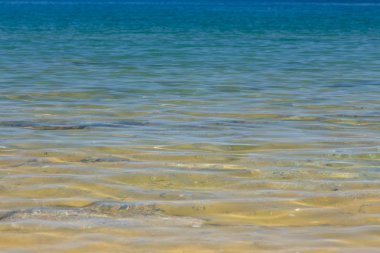 Mavi ve turuncu berrak su dokusu. Okyanusun arka planı ve güneş tarafından aydınlatılan deniz. Yumuşak dalgalar. Doğal su.