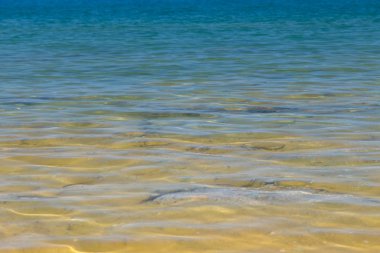 Mavi ve turuncu berrak su dokusu. Okyanusun arka planı ve güneş tarafından aydınlatılan deniz. Yumuşak dalgalar. Doğal su.