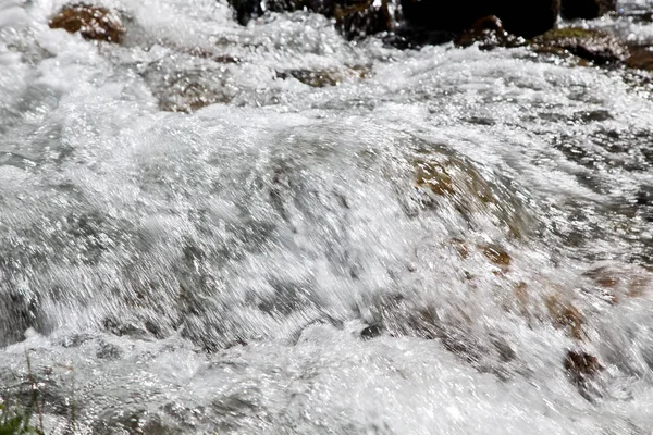 Vatten i den rasande floden. Vacker naturlig bakgrund av stenar och vatten. Textur av klart vatten och snabb flod. — Stockfoto