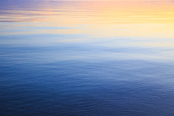 Textura de agua clara en azul y naranja. Fondo del océano y el mar retroiluminado por el sol. Ondas suaves. Agua natural — Foto de Stock