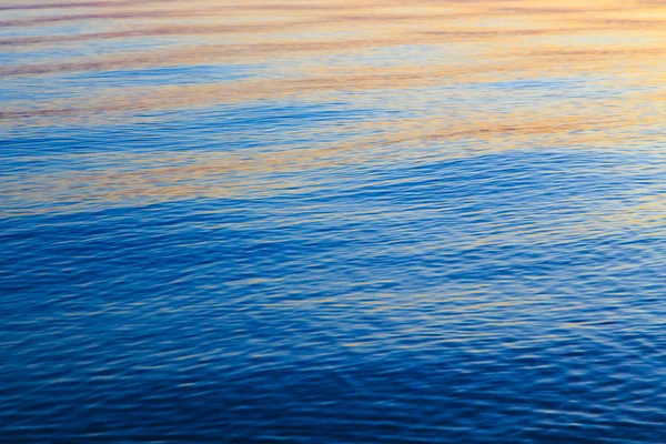 Struttura chiara dell'acqua in blu e arancione. Sullo sfondo dell'oceano e del mare retroilluminato dal sole. Onde morbide. Acqua naturale — Foto Stock