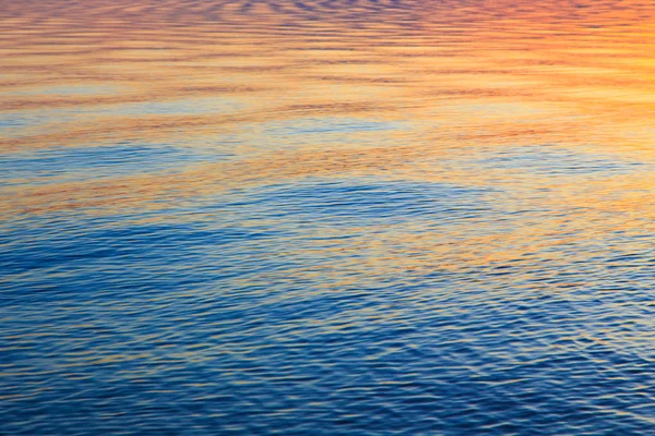 Textura clara da água em azul e laranja. Fundo do oceano e do mar iluminado pelo sol. Ondas suaves. Água natural — Fotografia de Stock