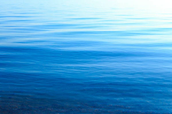 Textura clara da água em azul e laranja. Fundo do oceano e do mar iluminado pelo sol. Ondas suaves. Água natural — Fotografia de Stock