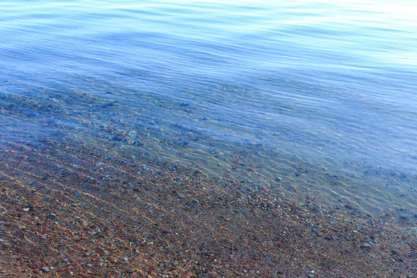 Heldere watertextuur in blauw en oranje. Achtergrond van de oceaan en de zee verlicht door de zon. Zachte golven. Natuurlijk water — Stockfoto