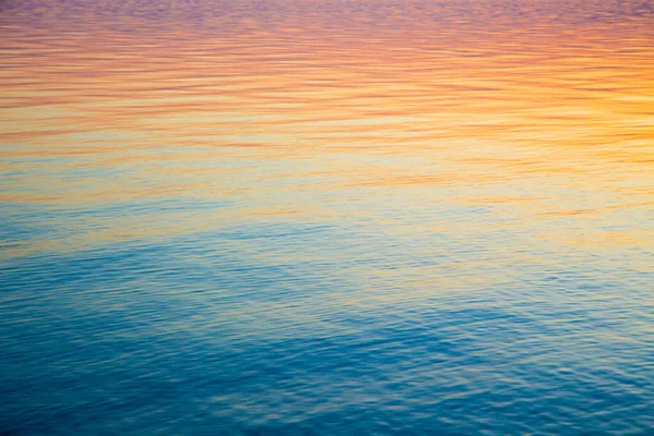 Textura clara da água em azul e laranja. Fundo do oceano e do mar iluminado pelo sol. Ondas suaves. Água natural — Fotografia de Stock