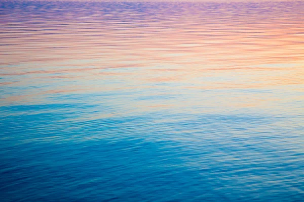 Textura de agua clara en azul y naranja. Fondo del océano y el mar retroiluminado por el sol. Ondas suaves. Agua natural — Foto de Stock