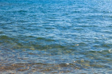 Mavi ve turuncu berrak su dokusu. Okyanusun arka planı ve güneş tarafından aydınlatılan deniz. Yumuşak dalgalar. Doğal su.