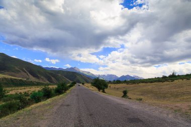 Güzel bahar ve yaz manzarası. Yeşil tepelerin arasındaki dağ yolu. Bereketli yeşil tepeler, yüksek dağlar. Yaz doğal arka plan.
