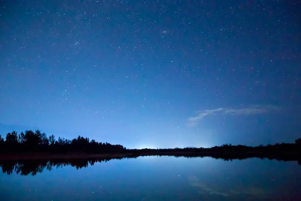 Starry sky and clouds. Night landscape, reflection of star paths in calm lake water.