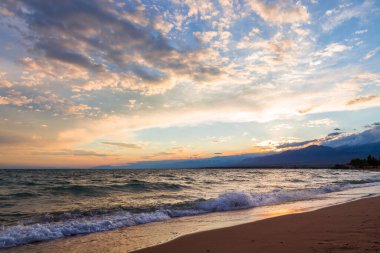 Gölün kenarında güzel bir gün batımı. Parlak bulutlar suya yansıyor. Doğada harika bir yaz akşamı. Kırgızistan.
