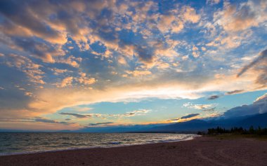 Gölün kenarında güzel bir gün batımı. Parlak bulutlar suya yansıyor. Doğada harika bir yaz akşamı. Kırgızistan.
