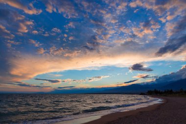 Gölün kenarında güzel bir gün batımı. Parlak bulutlar suya yansıyor. Doğada harika bir yaz akşamı. Kırgızistan.