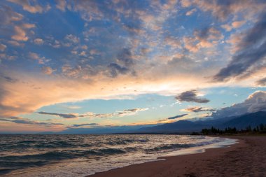 Gölün kenarında güzel bir gün batımı. Parlak bulutlar suya yansıyor. Doğada harika bir yaz akşamı. Kırgızistan.