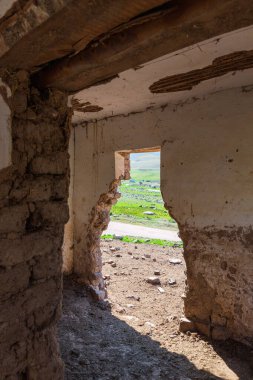 Terk edilmiş eski bir ev. Dağlar yıkılan açıklıktan görülebilir. Bina kerpiç ve ahşaptan yapılmıştır. Kırgızistan dağlarında bir ev.