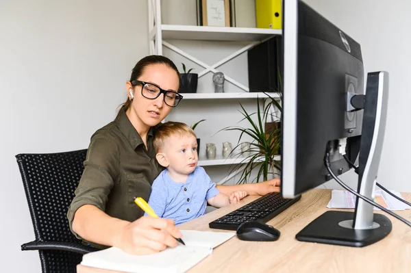 Mãe trabalha em casa escritório com criança em voltas — Fotografia de Stock