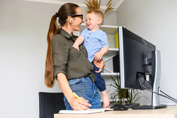 Mère travaille à la maison avec un enfant sur les bras — Photo