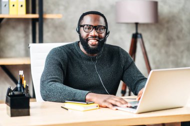 Kulaklık takmış, dizüstü bilgisayar kullanan Afro-Amerikalı bir adam.