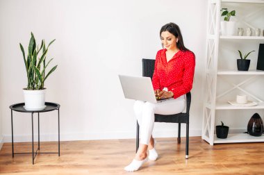 Çekici genç bir kadın evde dizüstü bilgisayarıyla oturuyor.