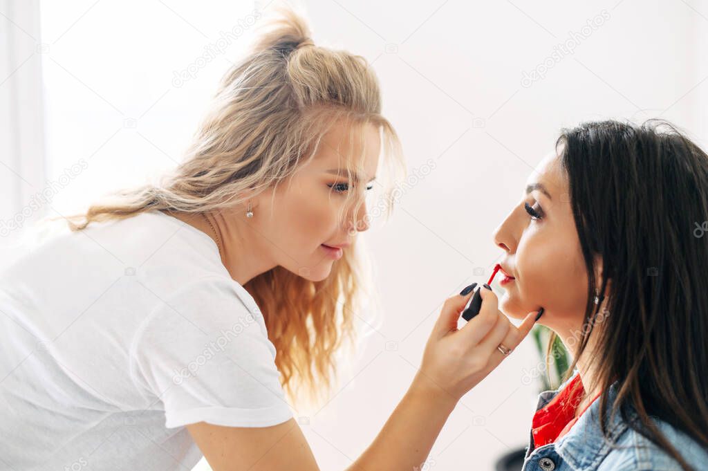 One girl put lipstick on lips of another girl