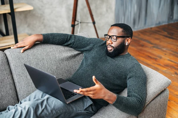 Afroameričan leží na pohovce s laptopem — Stock fotografie