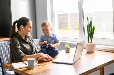 Genç anne evde dizüstü bilgisayarla çalışıyor.