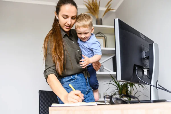 Mère travaille à la maison avec un enfant sur les bras — Photo