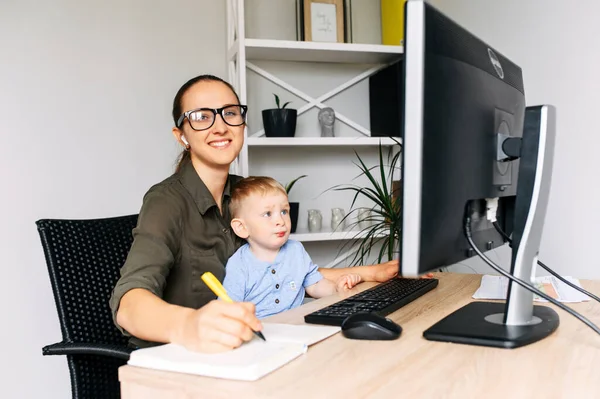 Mãe trabalha em casa escritório com criança em voltas — Fotografia de Stock