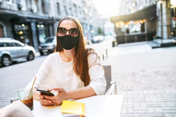 Donna in maschera medica con un telefono nel caffè — Foto Stock