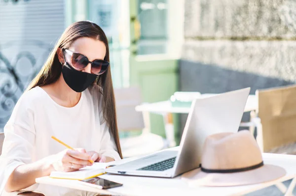 Жінка в медичній масці з ноутбуком в літньому кафе — стокове фото