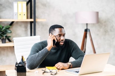 Bilgisayarla çalışırken telefonda konuşan adam.
