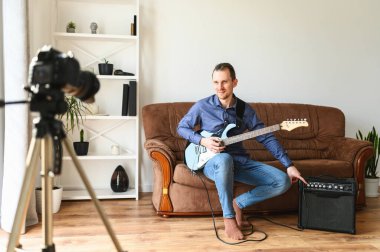 Bir adam elektro gitar çalmayı videoya kaydediyor.