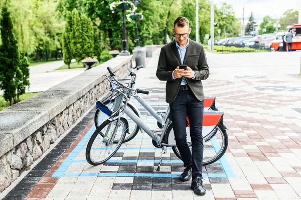 Un tipo en smart casual utilizando la aplicación para alquilar bicicleta de la ciudad —  Fotos de Stock