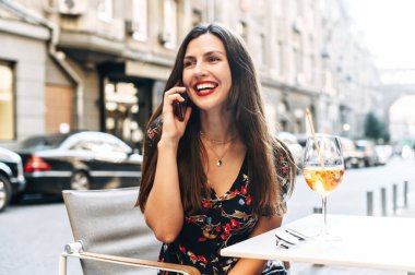 Güzel kız açık bir kafede telefonla konuşuyor.