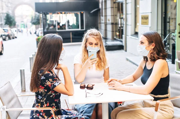 Дівчата в медичних масках проводять час у кафе на відкритому повітрі — стокове фото