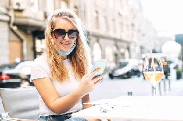 Chica en máscara médica pasa tiempo en un café al aire libre — Foto de Stock