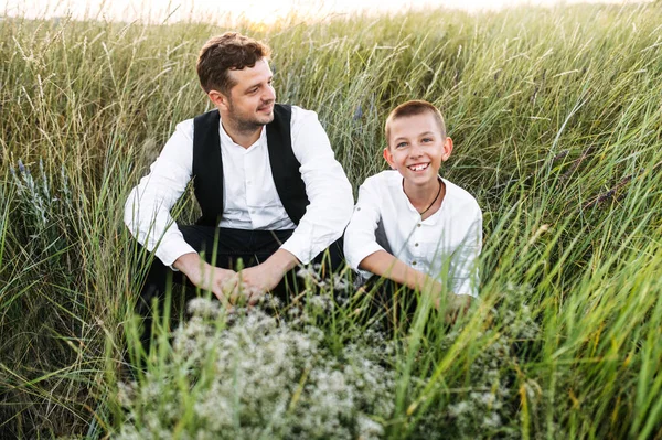 Le jeune père et le fils d'âge scolaire sont assis dans la prairie — Photo