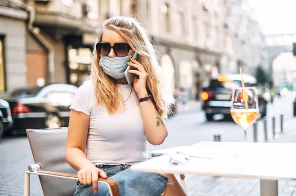 Дівчина в медичній масці проводить час у кафе на відкритому повітрі — стокове фото