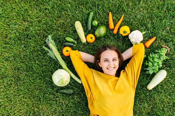 En kvinna ligger på gräs omgiven färska grönsaker — Stockfoto
