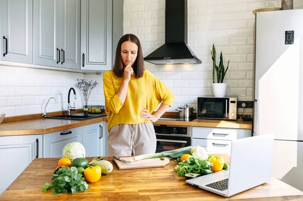 Uma menina fica de pé e confusa olha para os ingredientes — Fotografia de Stock