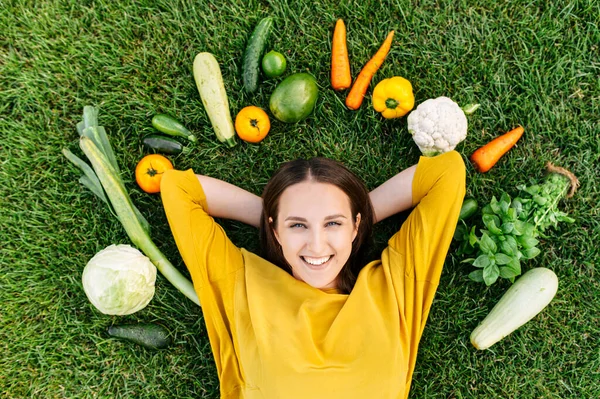 En kvinna ligger på gräs omgiven färska grönsaker — Stockfoto