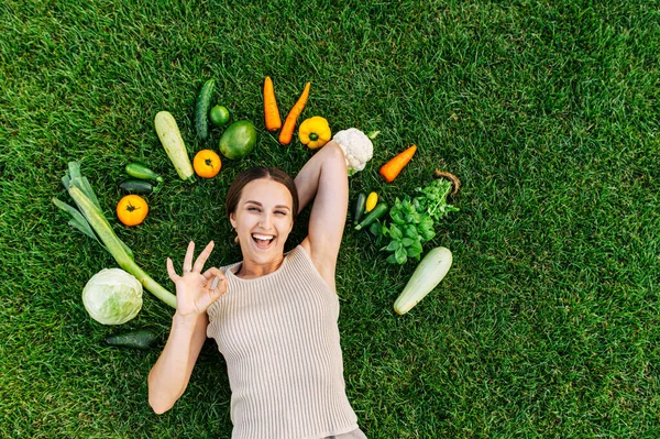 Una donna giace sull'erba circondata da verdure fresche — Foto Stock