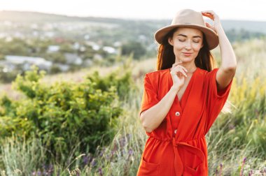 Şapkalı güzel bir kadın çiçek tarlasında yürüyor.