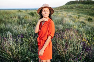 Şapkalı güzel bir kadın çiçek tarlasında yürüyor.