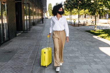 Dışarıda bavulu olan maskeli bir kadın.