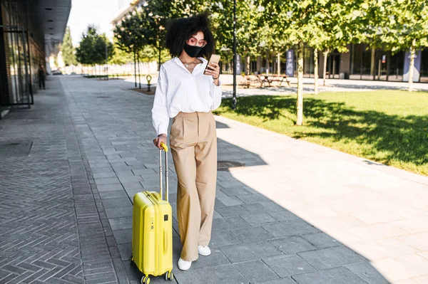 Una mujer con máscara y una maleta al aire libre — Foto de Stock